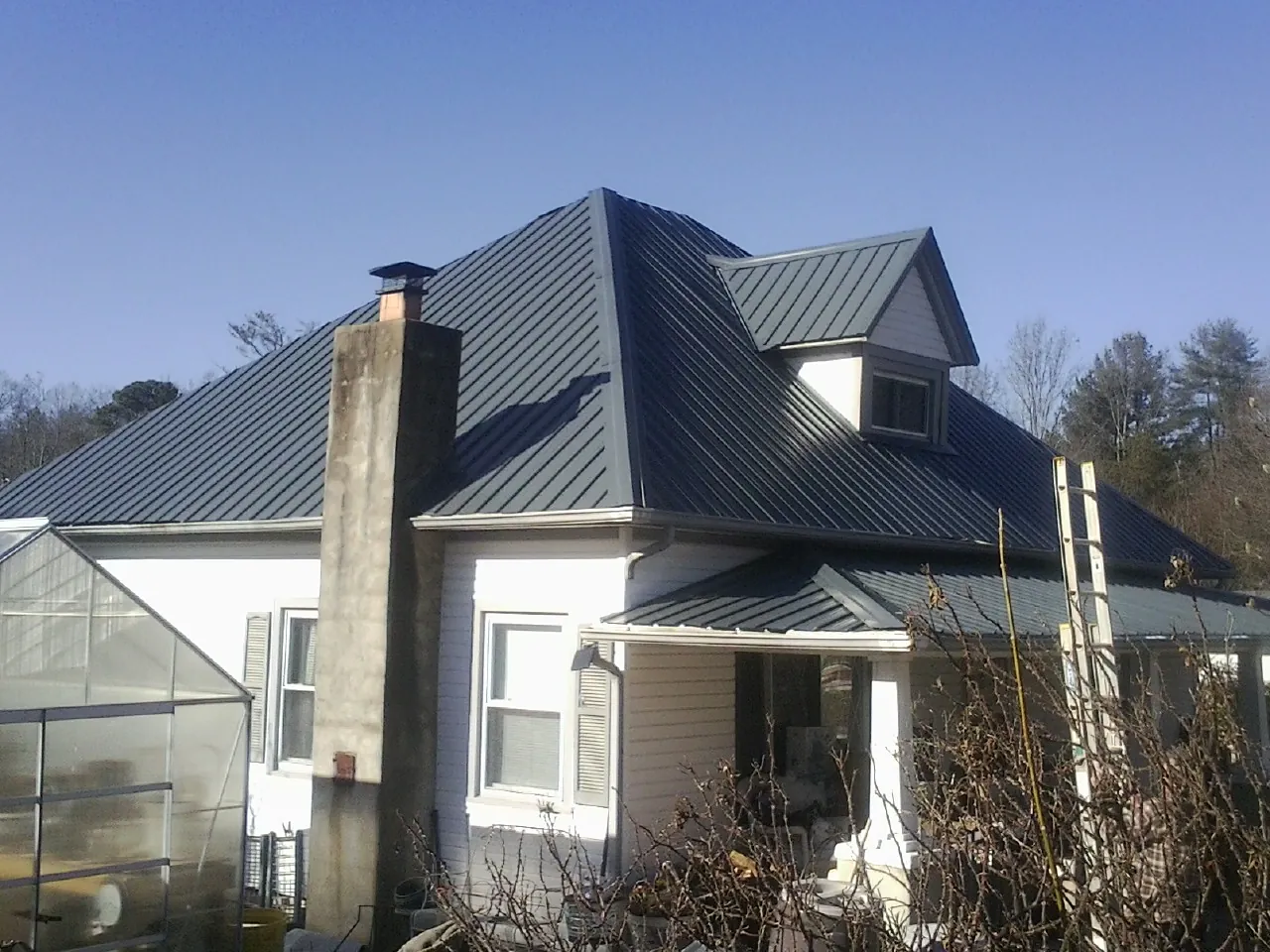 Dark blue standing seam metal roof on a white farmhouse with dormer — Slate & Tile Roof Repair by Roofing Brothers in Forest Hill