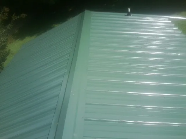 New green metal panels meeting at the ridge of a roof — Flat Roof Repair work by our crew in Forest Hill