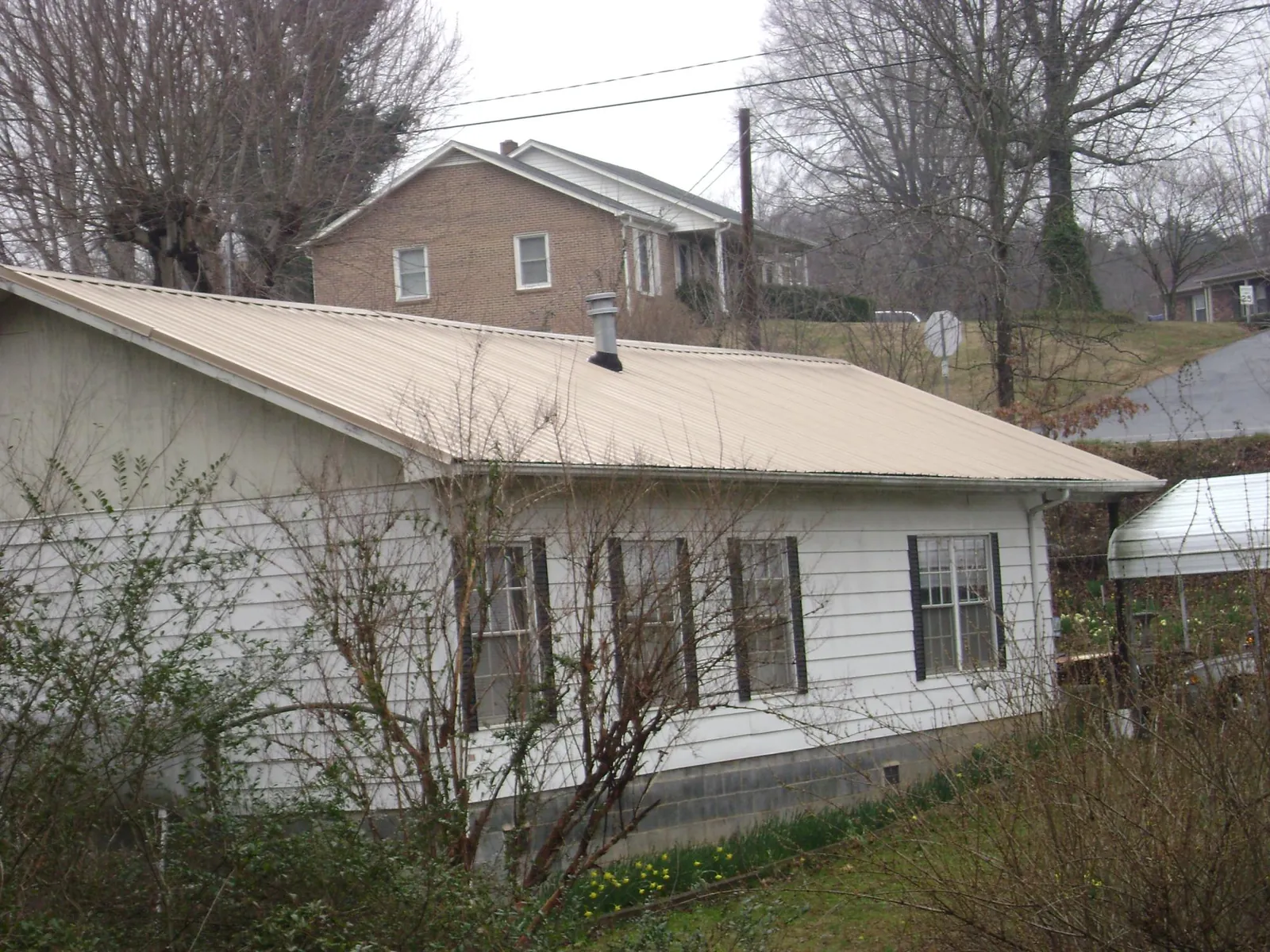 Tan metal roof on a white sided house set into a hillside — Commercial Roofing by Roofing Brothers in Forest Hill
