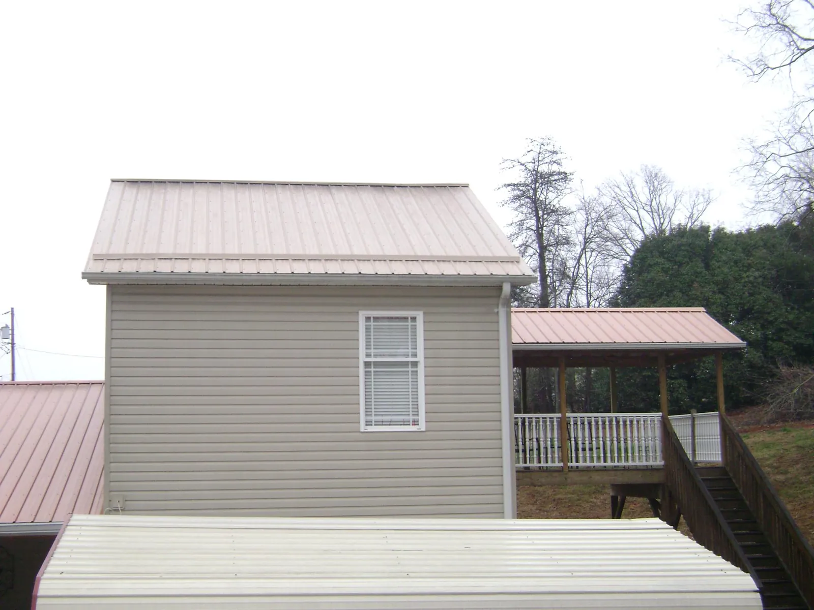 Tan metal roofs on a two story addition and attached porch, from a Roof Replacement job in Forest Hill